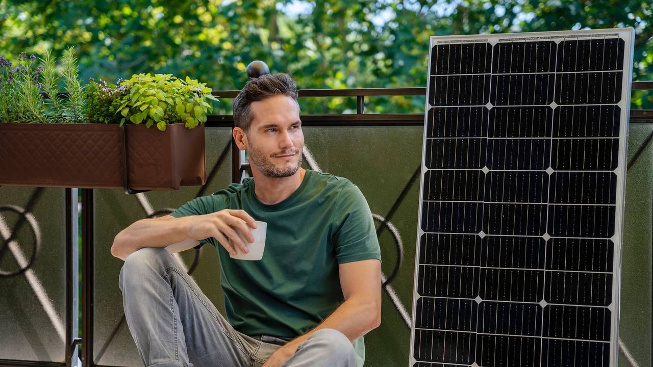 Mann mit Kaffee, Solarmodul und Pflanzen auf Balkon