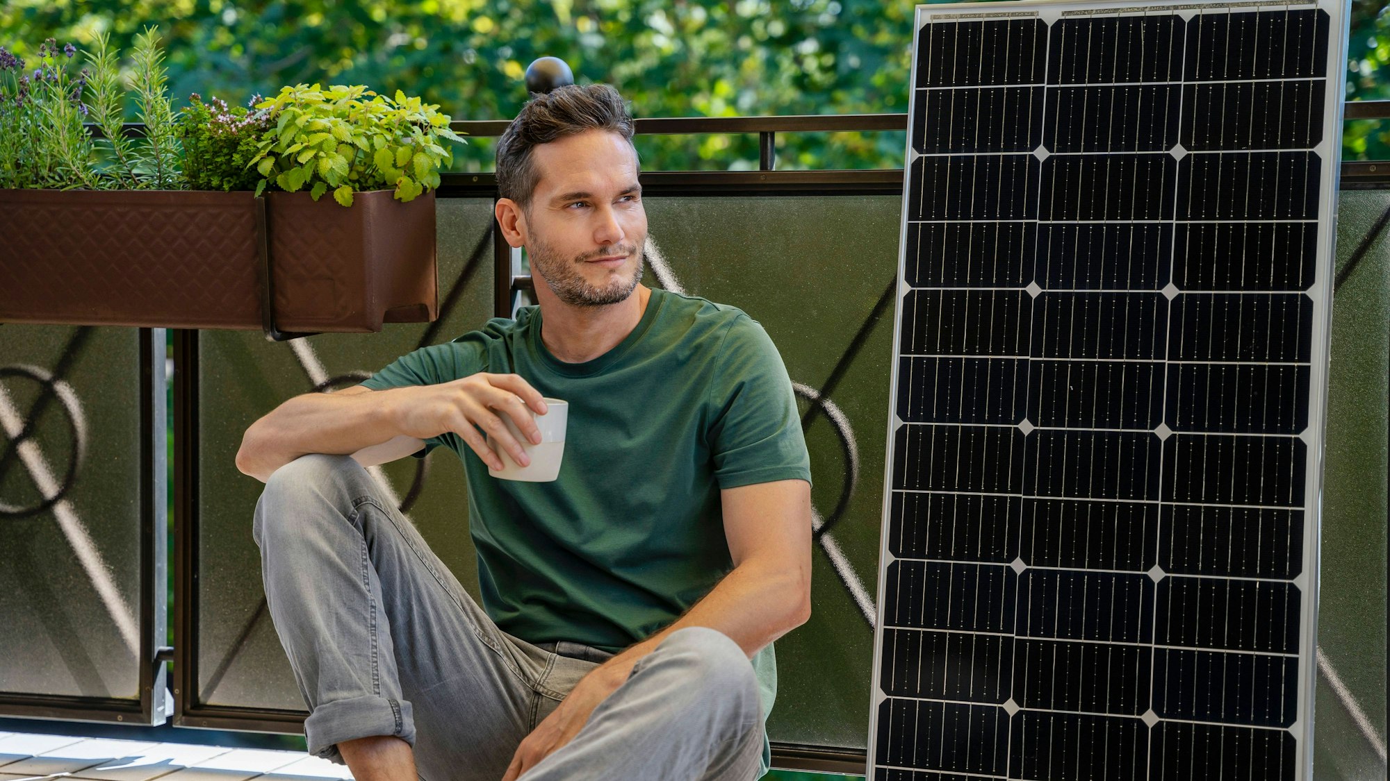 Mann mit Kaffee, Solarmodul und Pflanzen auf Balkon