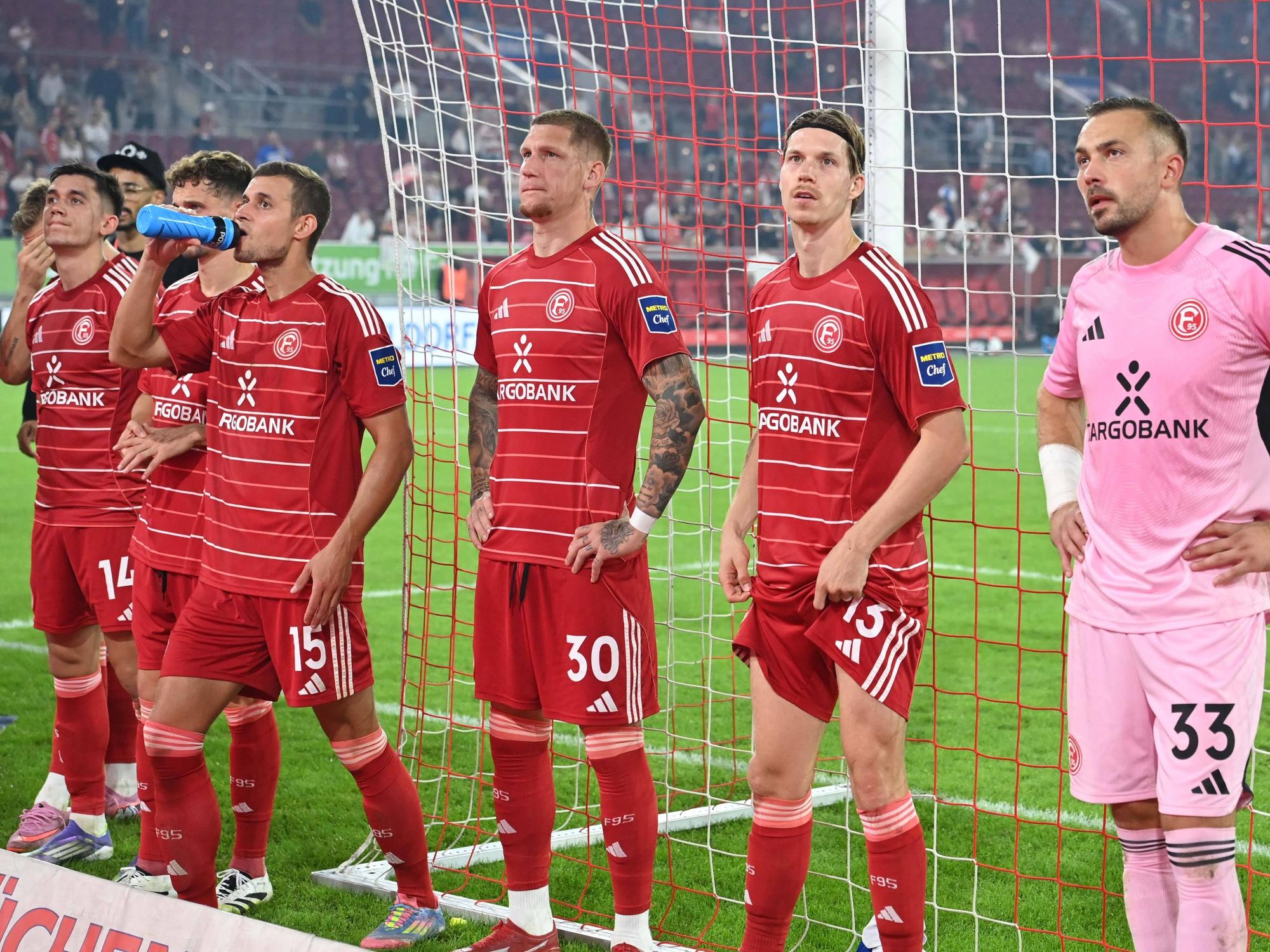 Die Spieler von Fortuna Düsseldorf stehen vor der Fankurve und sehen enttäuscht aus.