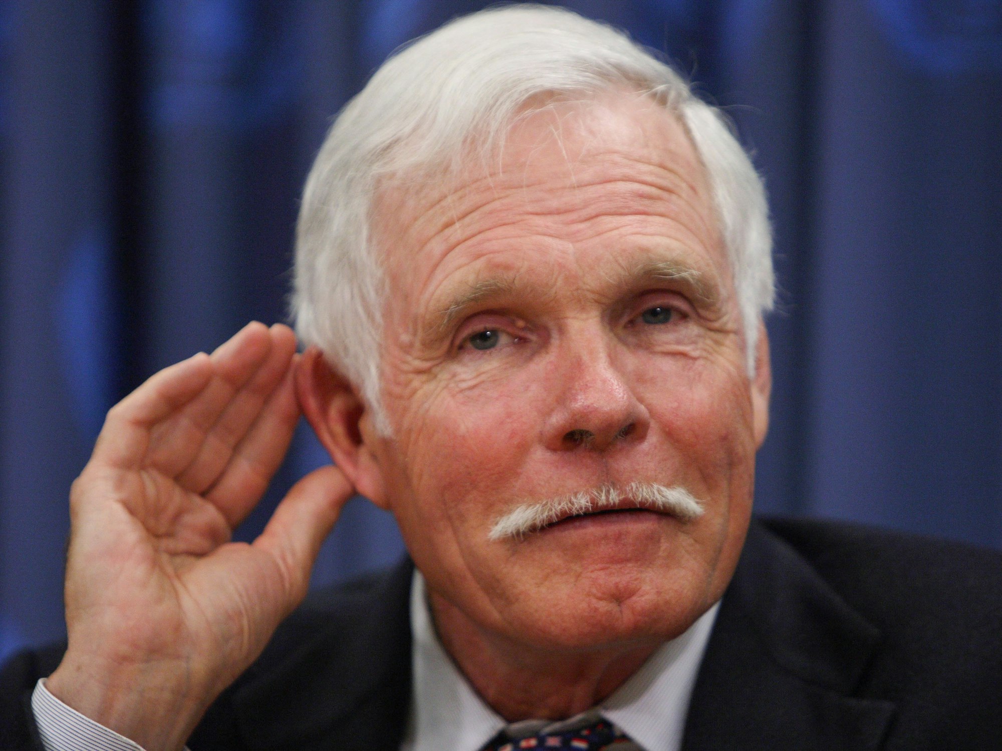 Ted Turner legt eine Hand ans Ohr.