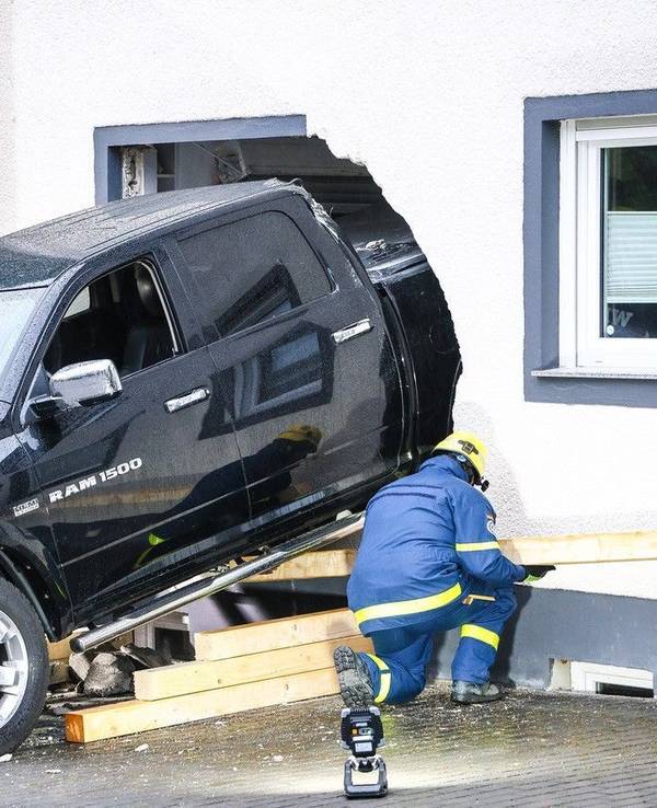 Ein Mitarbeiter des Technischen Hilfswerk (THW) ist an einem Fahrzeug beschäftigt, das die Fassade eines Wohnhauses durchbrochen hat.