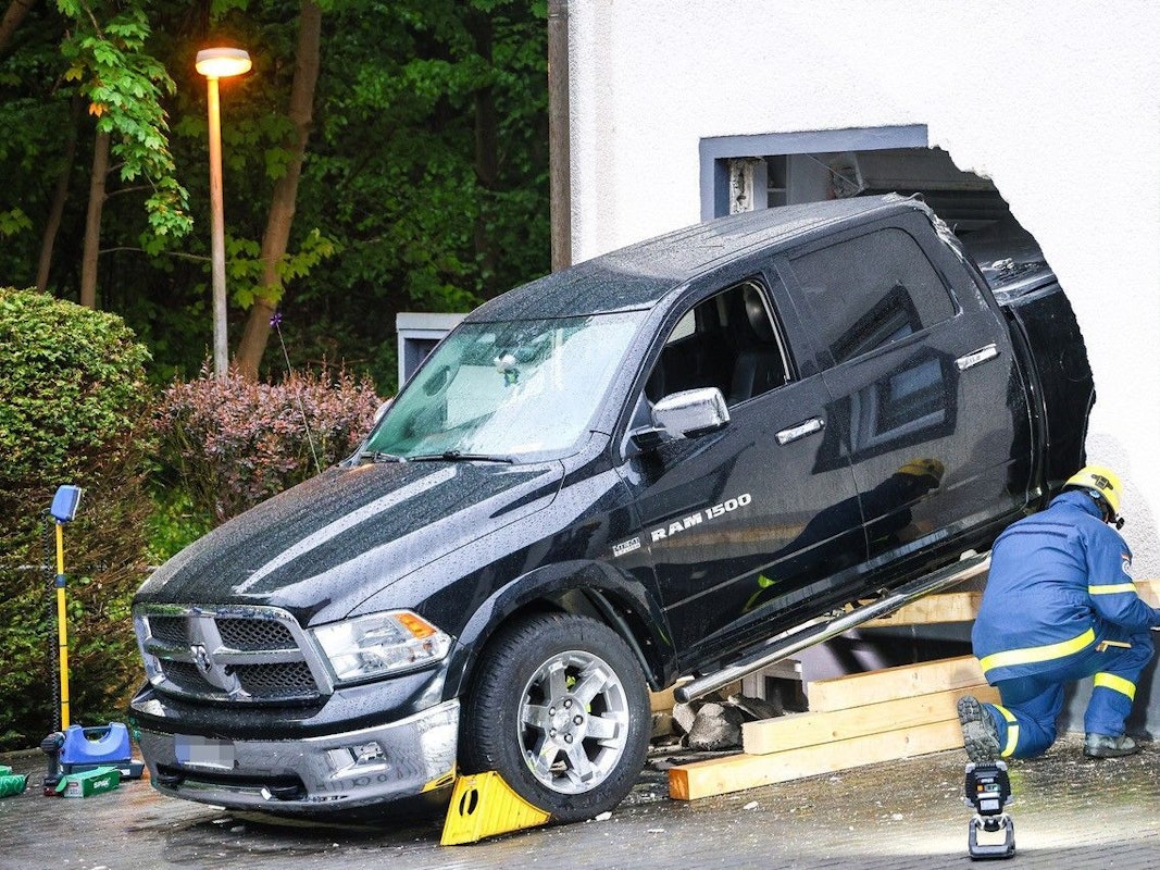 Ein Mitarbeiter des Technischen Hilfswerk (THW) ist an einem Fahrzeug beschäftigt, das die Fassade eines Wohnhauses durchbrochen hat.