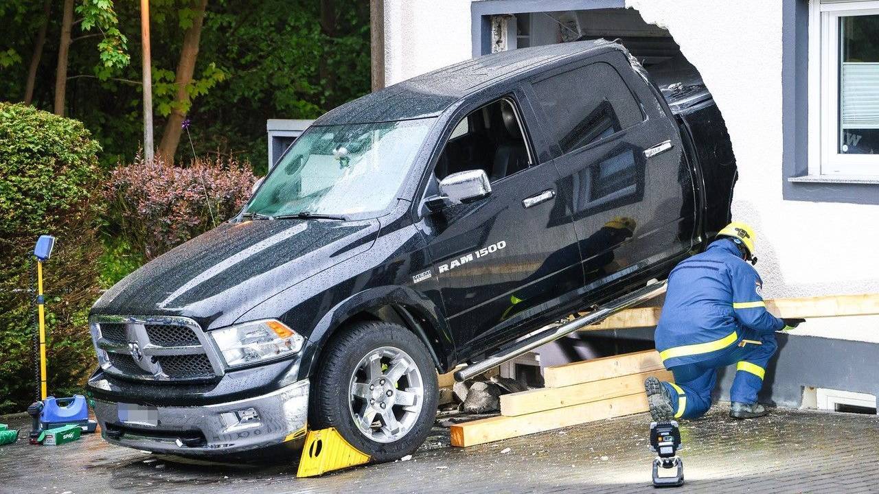 Ein Mitarbeiter des Technischen Hilfswerk (THW) ist an einem Fahrzeug beschäftigt, das die Fassade eines Wohnhauses durchbrochen hat.