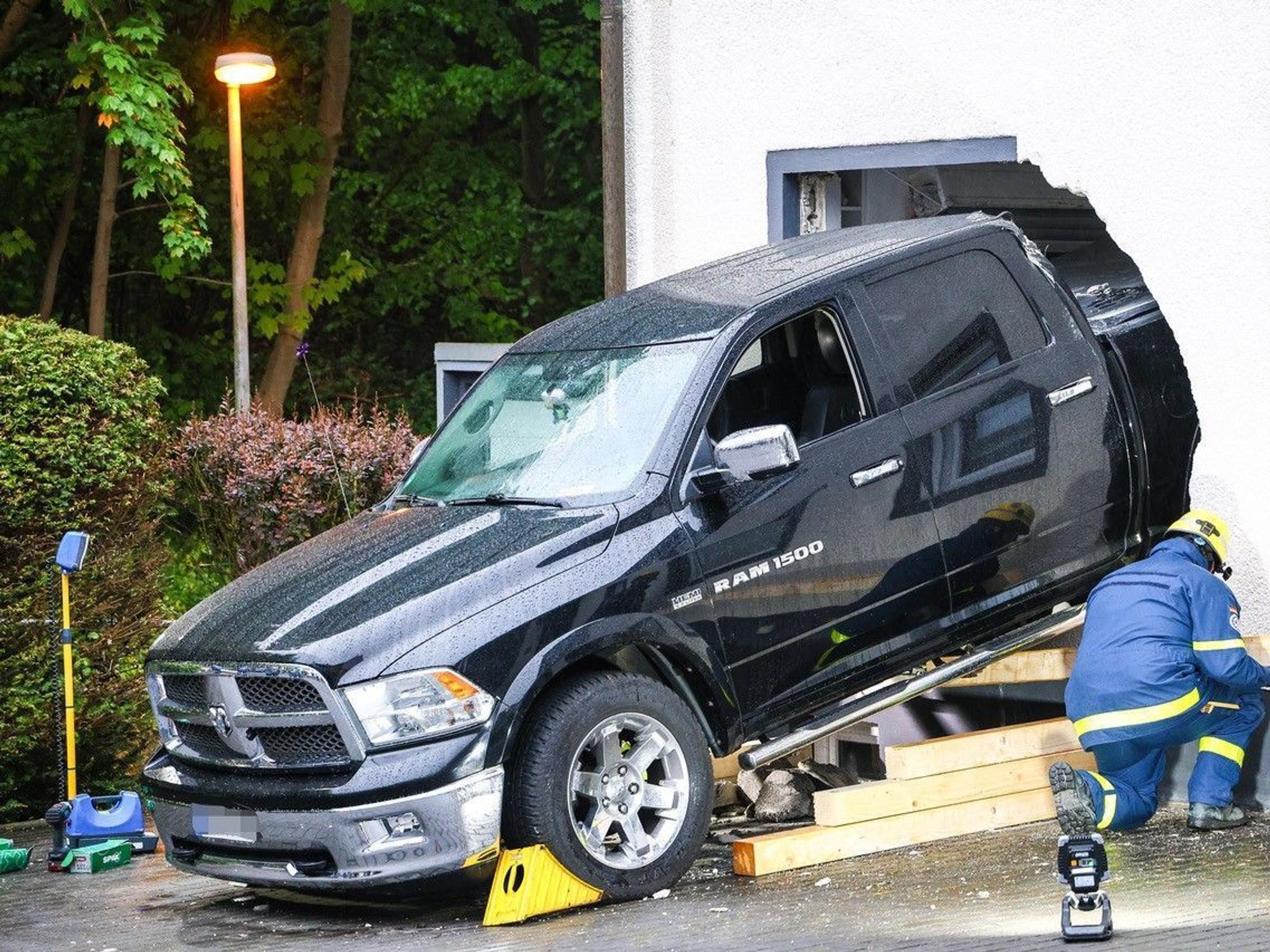 Ein Mitarbeiter des Technischen Hilfswerk (THW) ist an einem Fahrzeug beschäftigt, das die Fassade eines Wohnhauses durchbrochen hat.