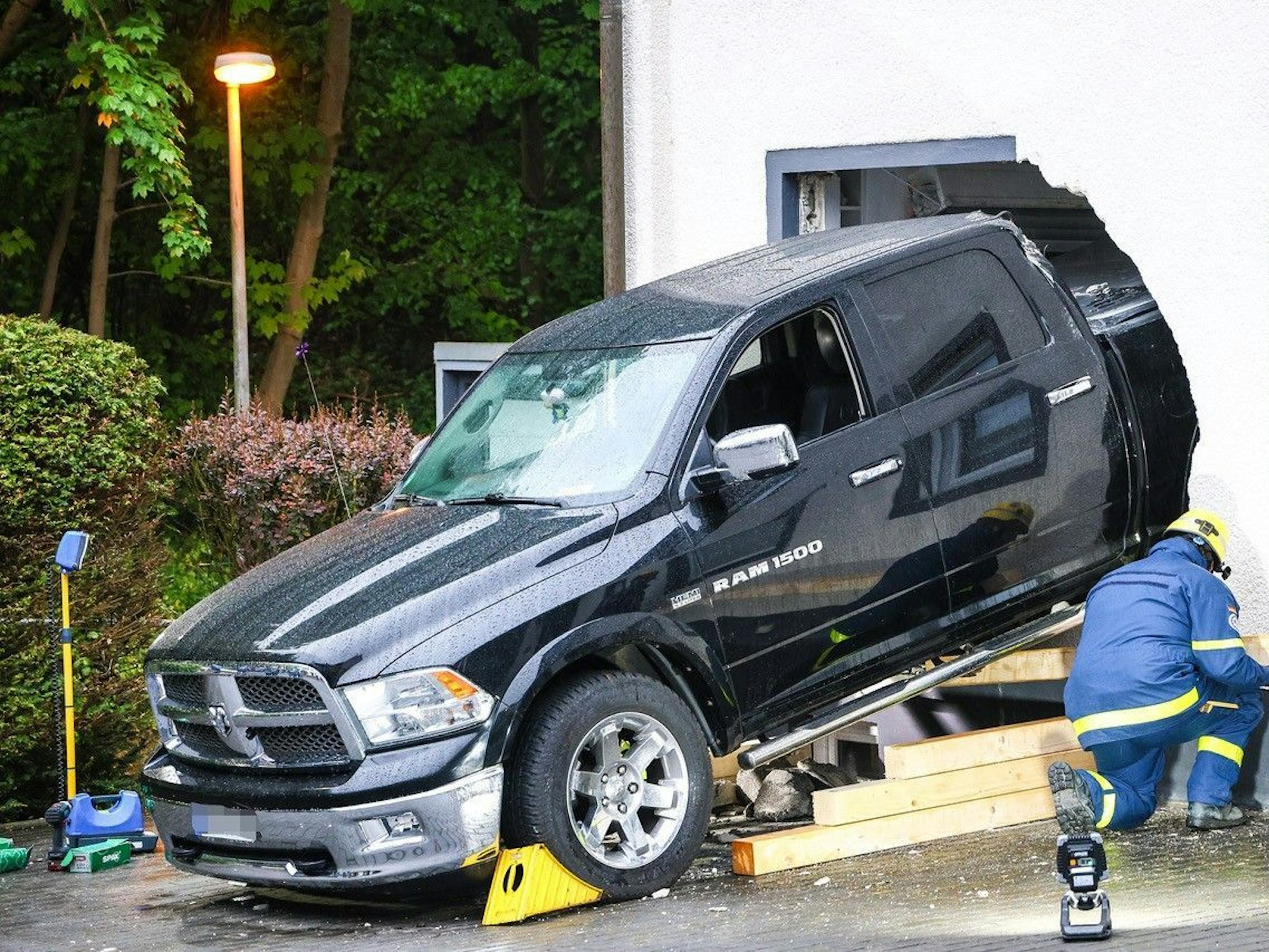 Ein Mitarbeiter des Technischen Hilfswerk (THW) ist an einem Fahrzeug beschäftigt, das die Fassade eines Wohnhauses durchbrochen hat.