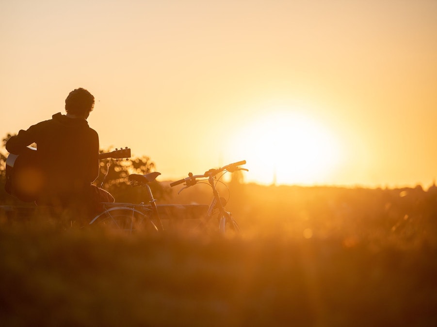 Mann spielt im Licht der aufgehenden Morgensonne Gitarre