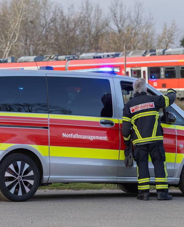 Ein Auto vom Notfallmanagement steht an einer Bahnstrecke, auf der ein Zug fährt.