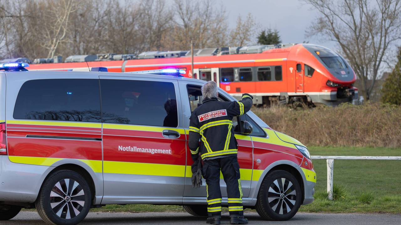 Ein Auto vom Notfallmanagement steht an einer Bahnstrecke, auf der ein Zug fährt.