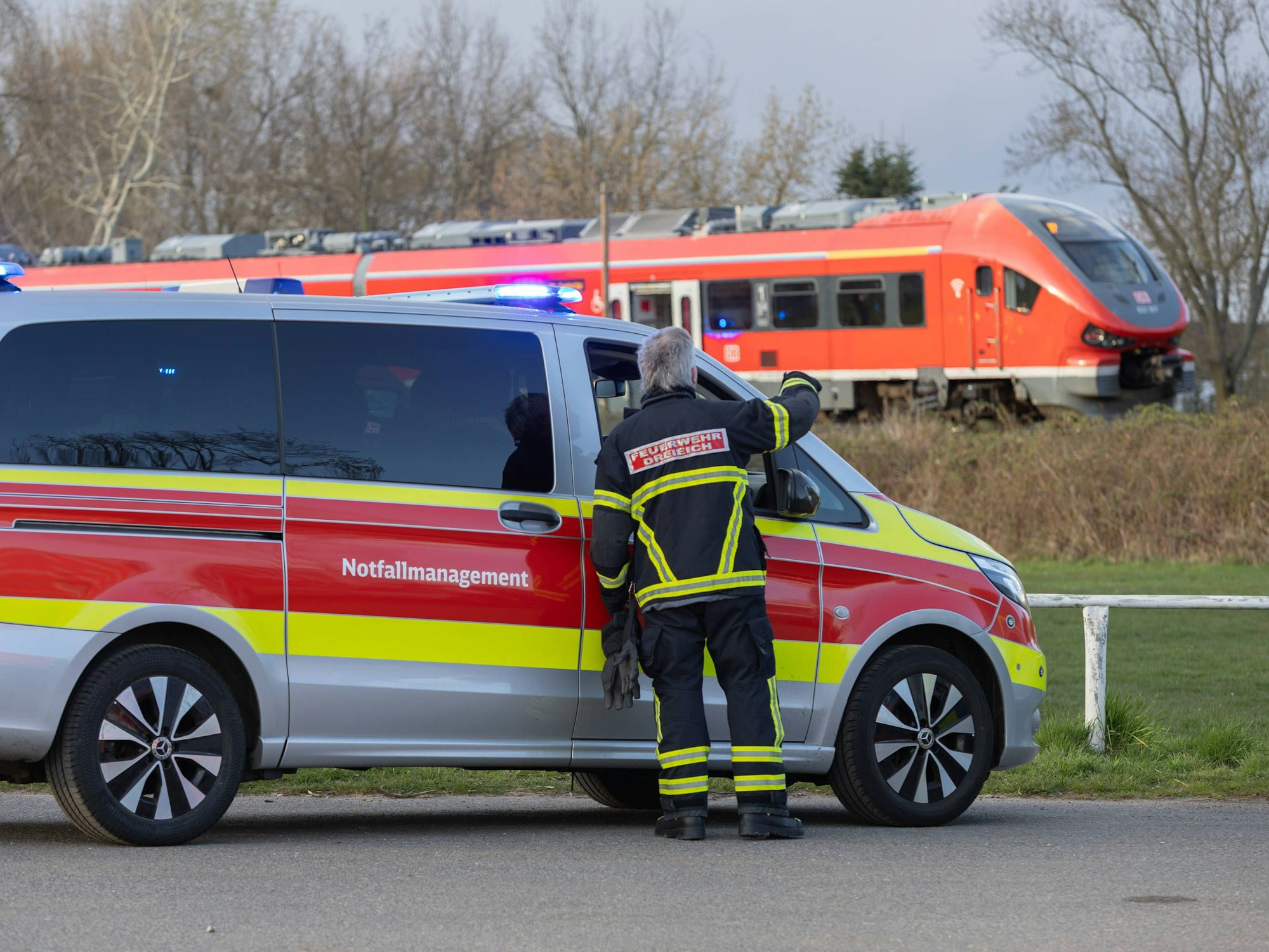 Ein Auto vom Notfallmanagement steht an einer Bahnstrecke, auf der ein Zug fährt.