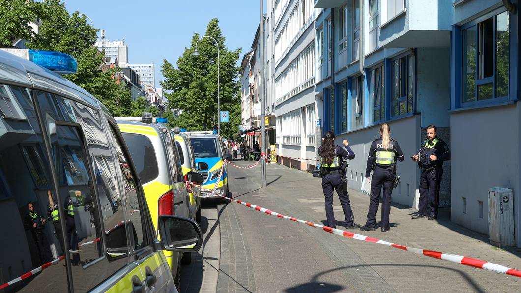 Drei Einsatzkräfte der Polizei stehen vor einem Haus, dessen Eingangsbereich mit Flatterband abgesperrt wurde.