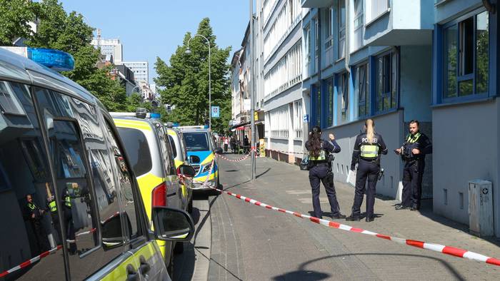 Drei Einsatzkräfte der Polizei stehen vor einem Haus, dessen Eingangsbereich mit Flatterband abgesperrt wurde.