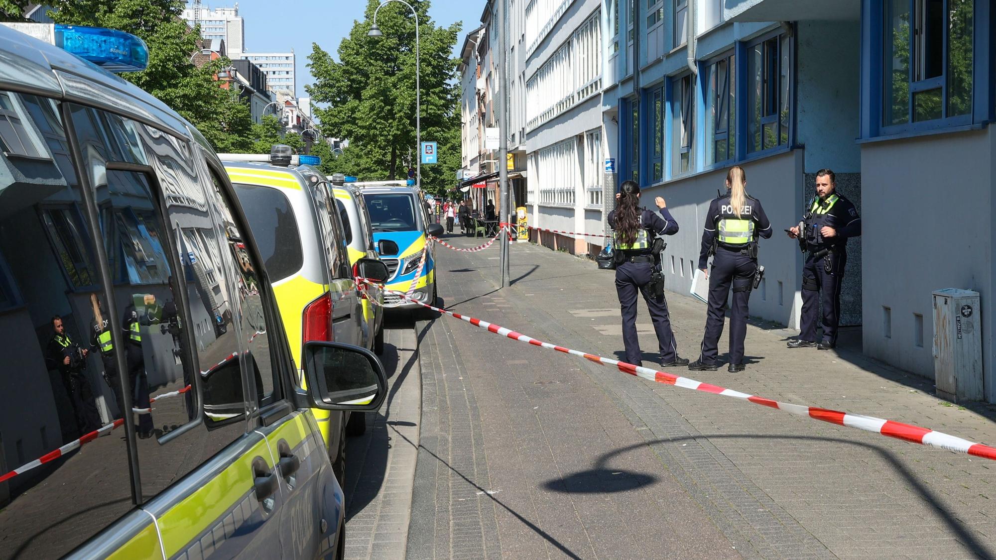 Die Polizei hat einen Bürgersteig abgesperrt, Polizeifahrzeuge parken vor dem Haus, drei Einsatzkräfte stehen vor der Haustür.