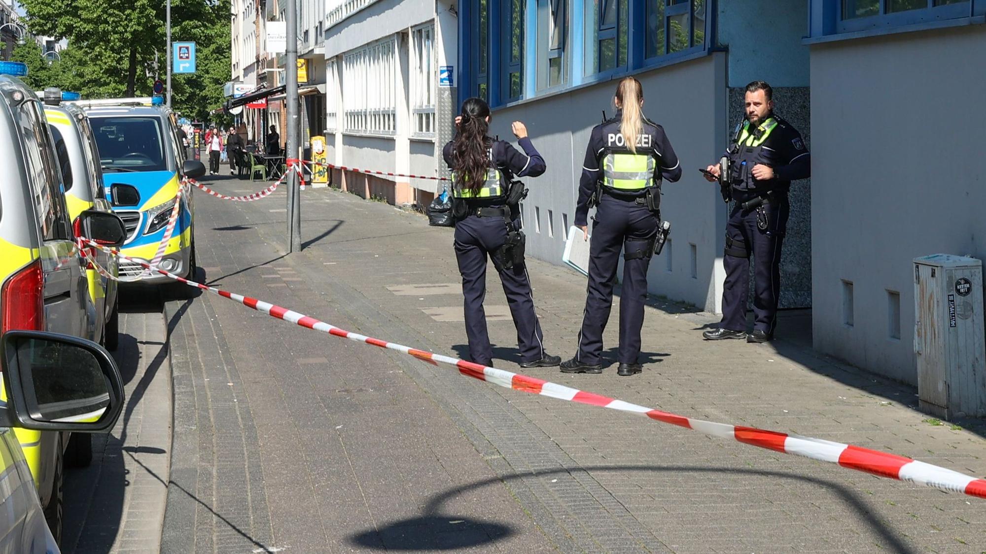 Drei Einsatzkräfte der Polizei stehen vor einem Haus, dessen Eingangsbereich mit Flatterband abgesperrt wurde.