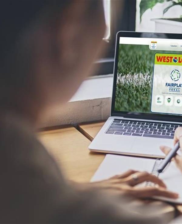 Eine Frau sitzt an einem Tisch und schaut auf ihren Laptop. Der Laptop zeigt die Internetseite des WestLotto Fairplay-Pokals.