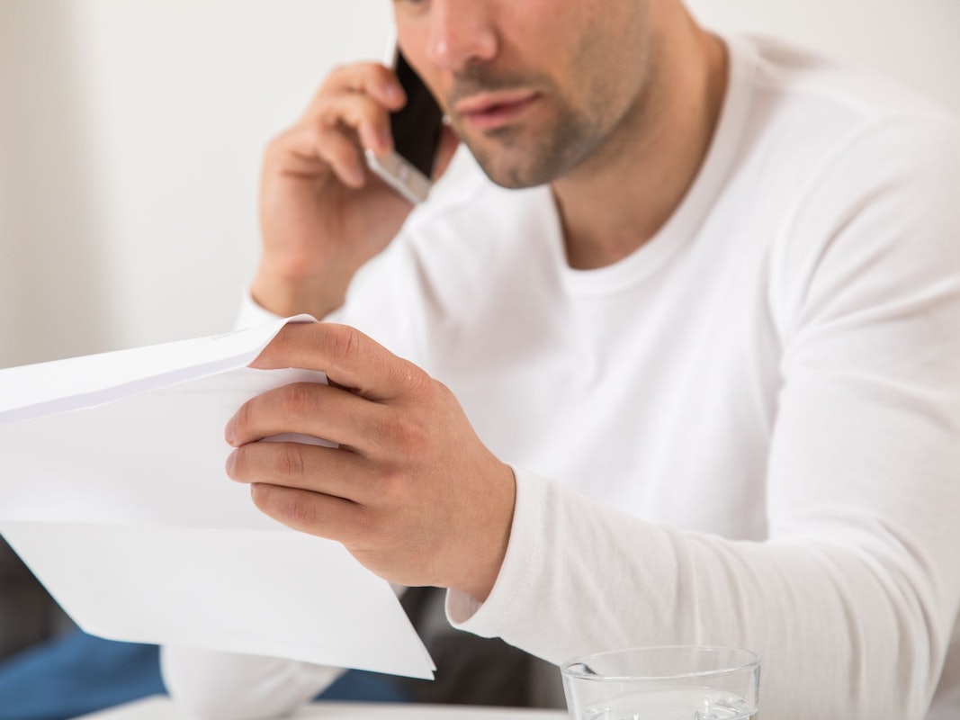 Mann telefoniert mit einem Brief in der Hand