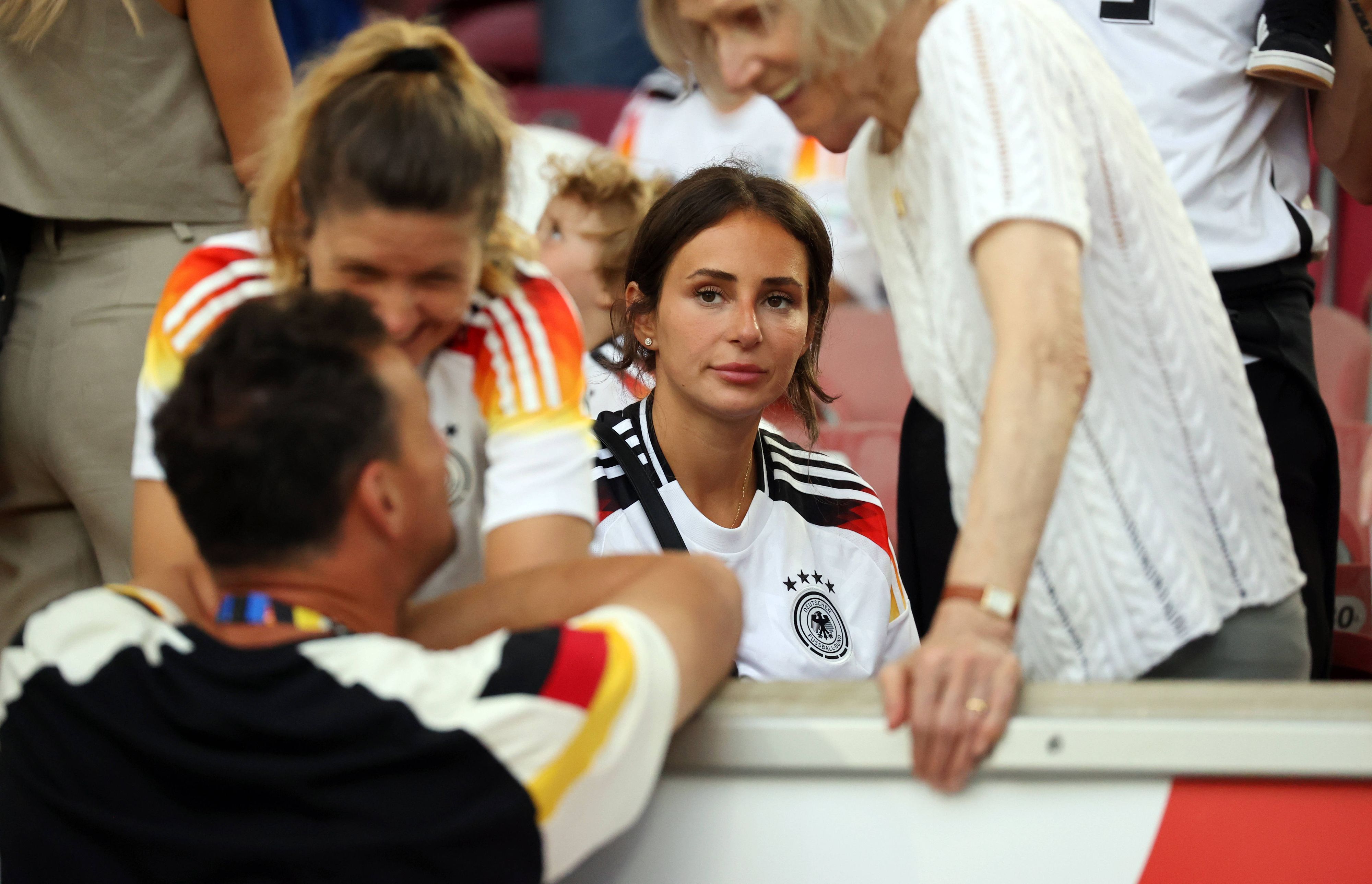 Antons Frau Jenny sitzt auf der Tribüne bei einem Spiel der deutschen Nationalmannschaft.