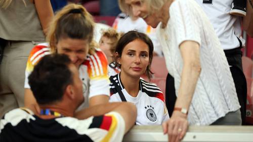 Antons Frau Jenny sitzt auf der Tribüne bei einem Spiel der deutschen Nationalmannschaft.