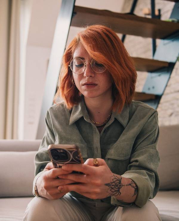 Eine junge Frau sitzt ernst mit dem Smartphone auf der Couch