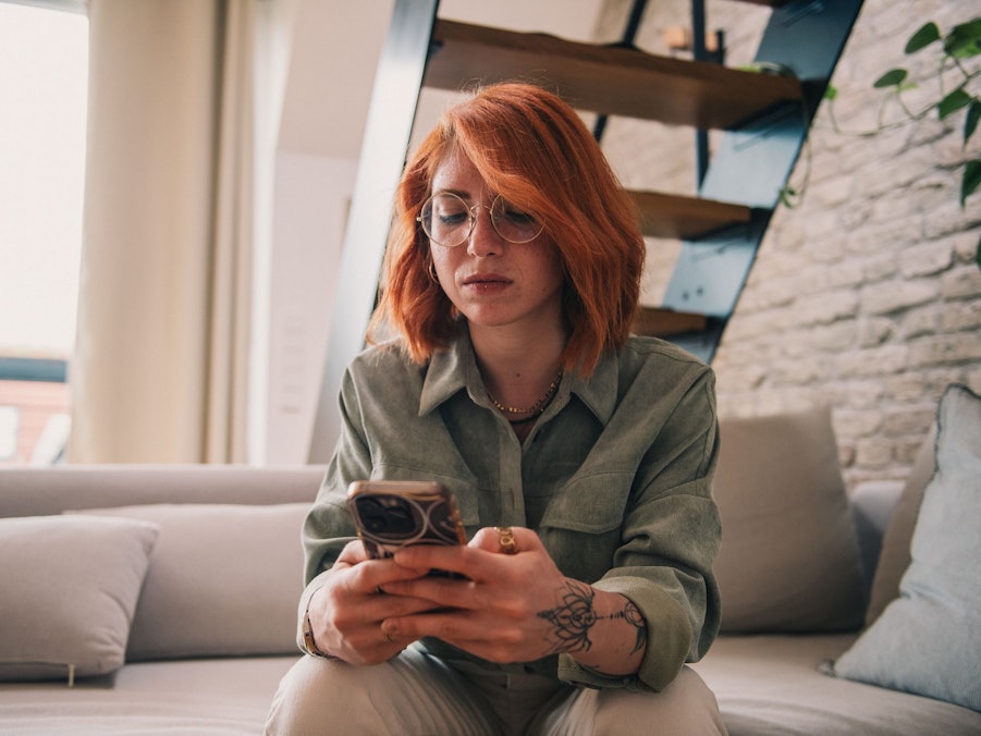 Eine junge Frau sitzt ernst mit dem Smartphone auf der Couch