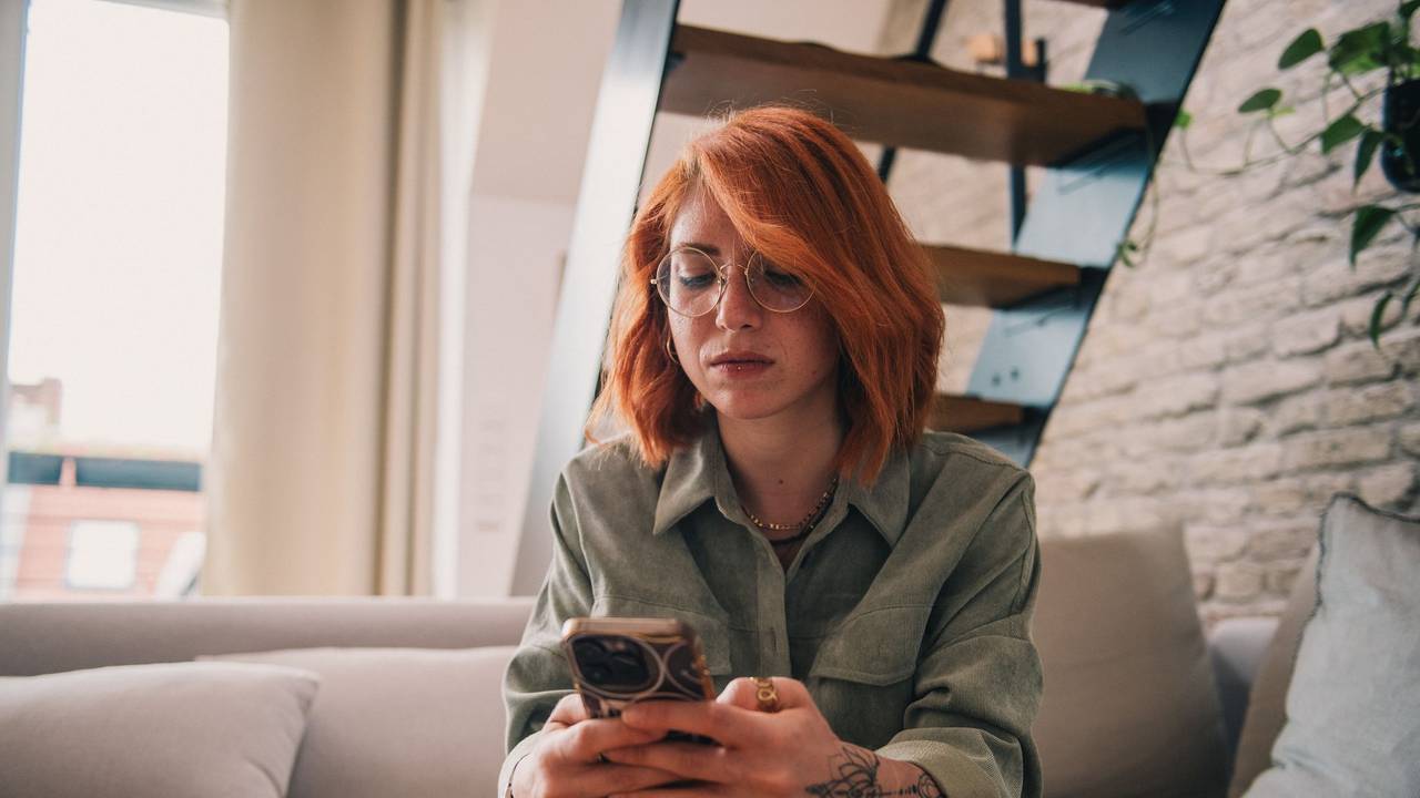 Eine junge Frau sitzt ernst mit dem Smartphone auf der Couch