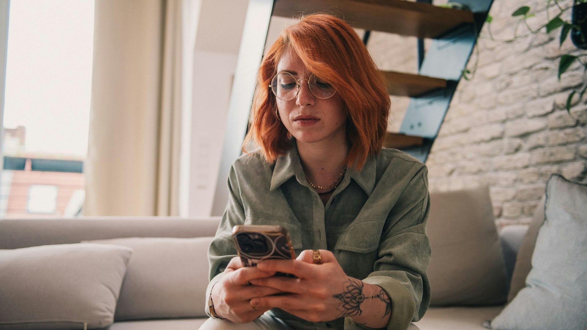 Eine junge Frau sitzt ernst mit dem Smartphone auf der Couch