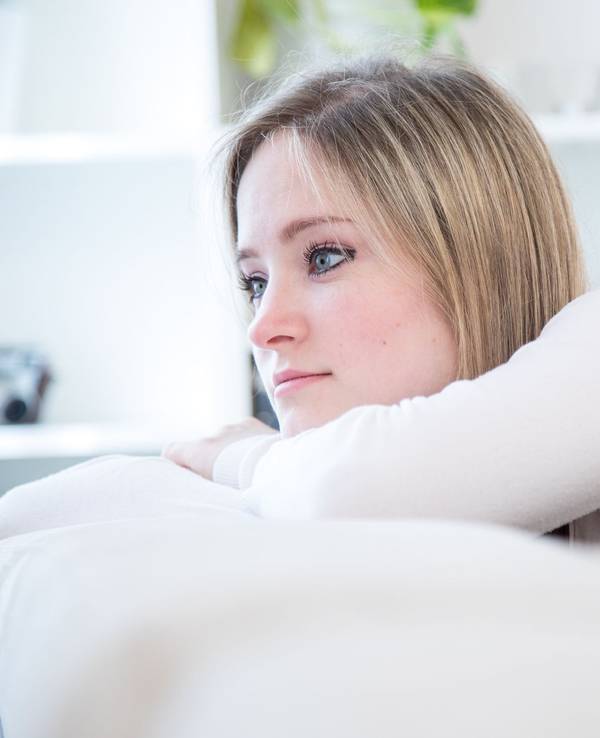 Eine junge Frau lehnt nachdenklich auf dem Sofa