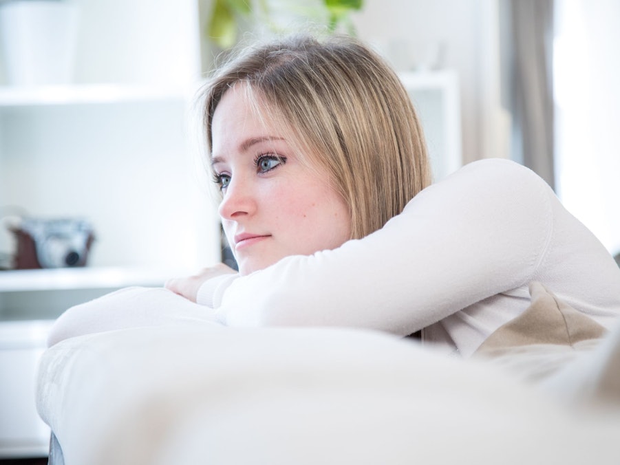 Eine junge Frau lehnt nachdenklich auf dem Sofa