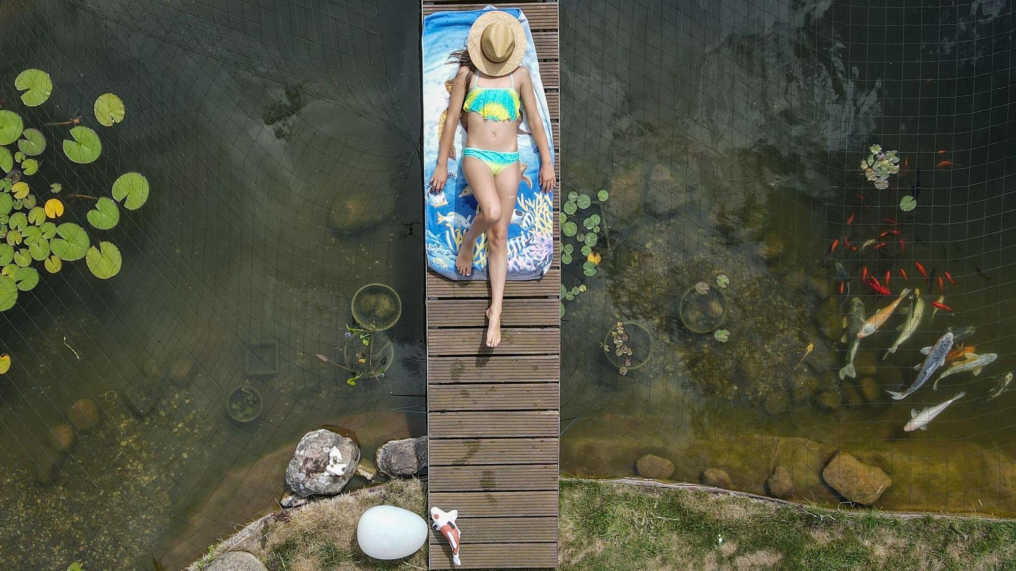 Mädchen sonnt sich auf einer Brücke über einem Gartenteich