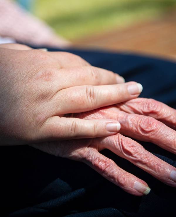 Hand einer Pflegefachkraft liegt auf Hand eienr Seniorin