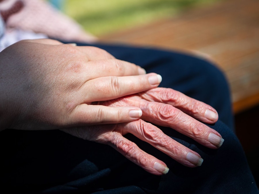 Hand einer Pflegefachkraft liegt auf Hand eienr Seniorin