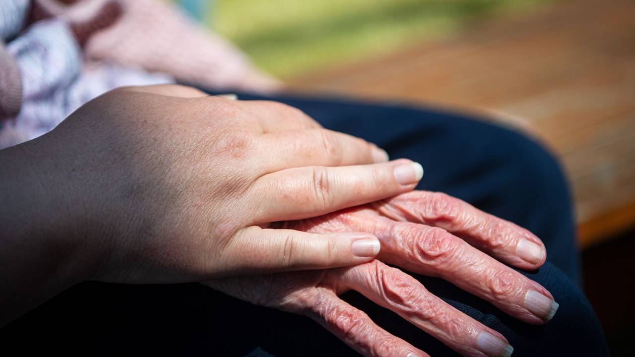 Hand einer Pflegefachkraft liegt auf Hand eienr Seniorin