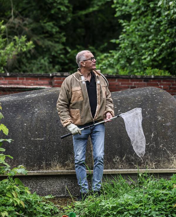 Ralf Atzorn, Vorsitzender des Kölner Imkerverbands, steht mit einem Kescher in einem Garten. Atzorn beseitigt Nester der Asiatischen Hornisse.