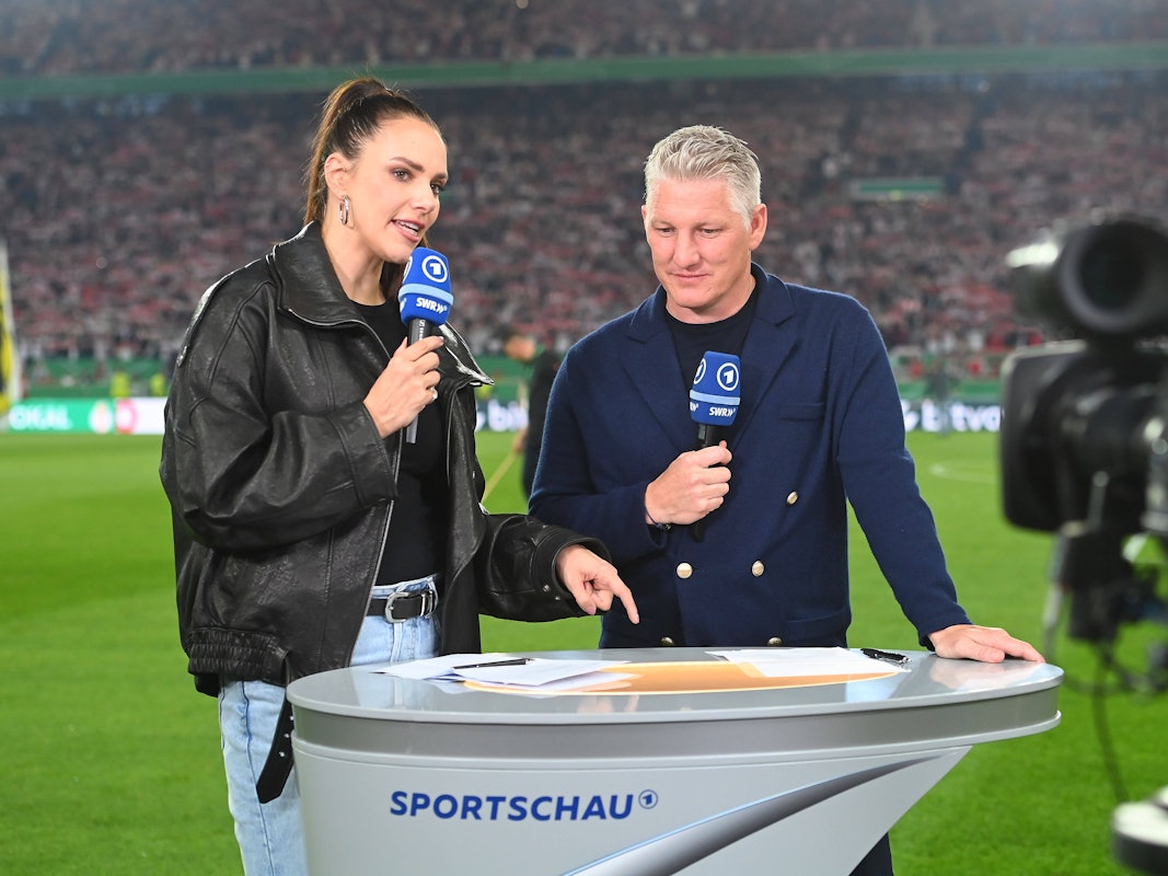 ARD-Moderatorin Esther Sedlaczek und Bastian Schweinsteiger halten bei einer TV-Übertragung Mikrofone in der Hand.