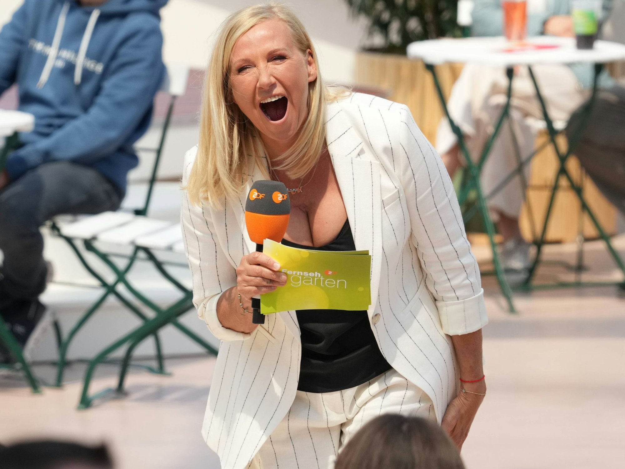 Andrea „Kiwi“ Kiewel lacht im ZDF Fernsehgarten, dabei hält sie Mikro und einen Zettel in der Hand.