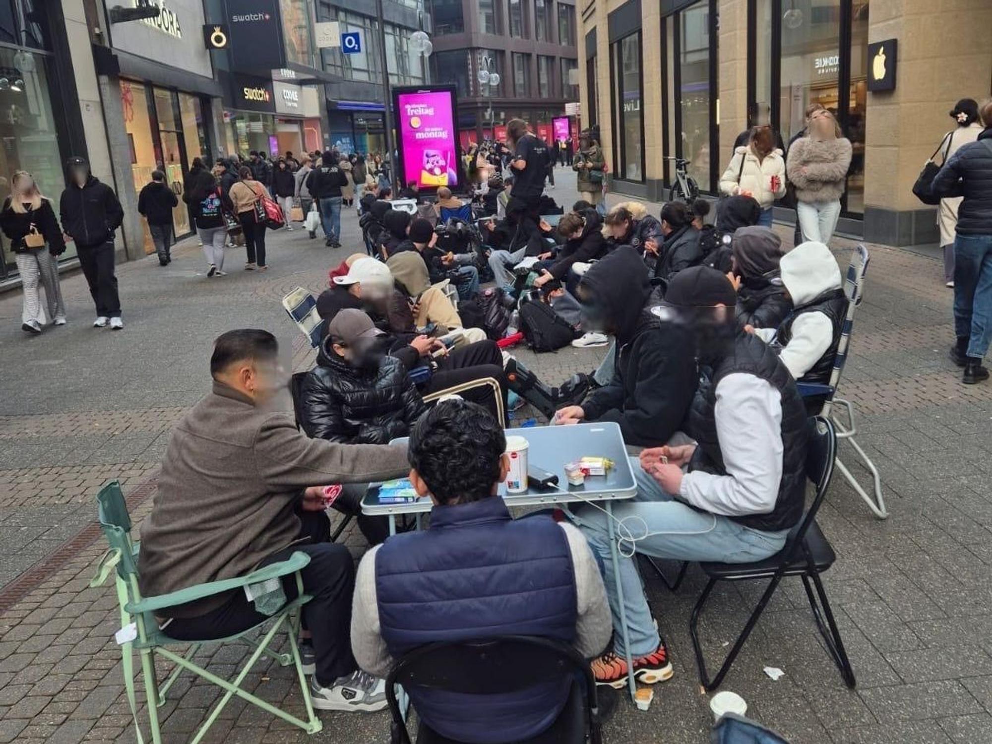 Menschen sitzen in einer Schlange in der Fußgängerzone.