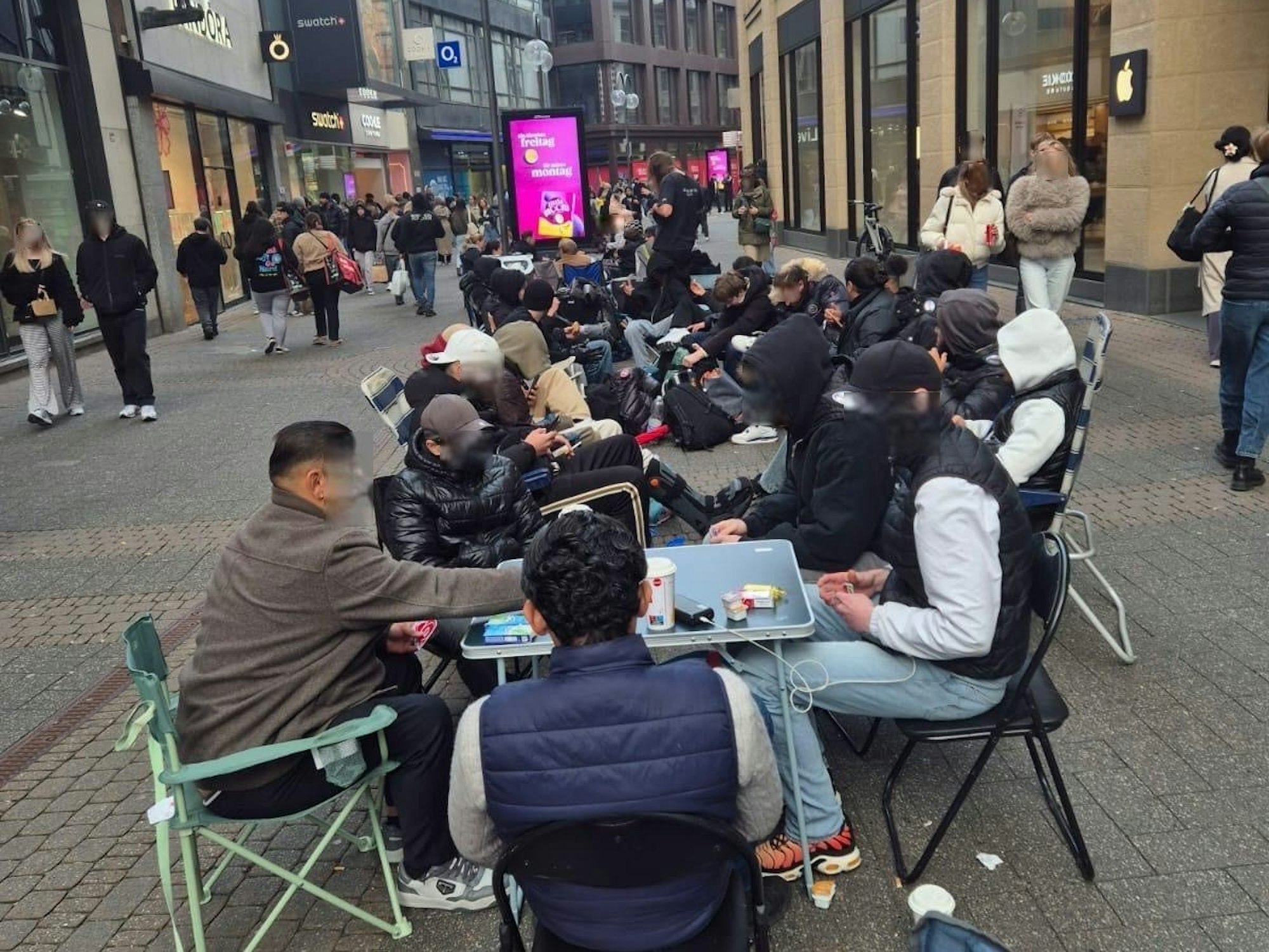 Menschen sitzen in einer Schlange in der Fußgängerzone.