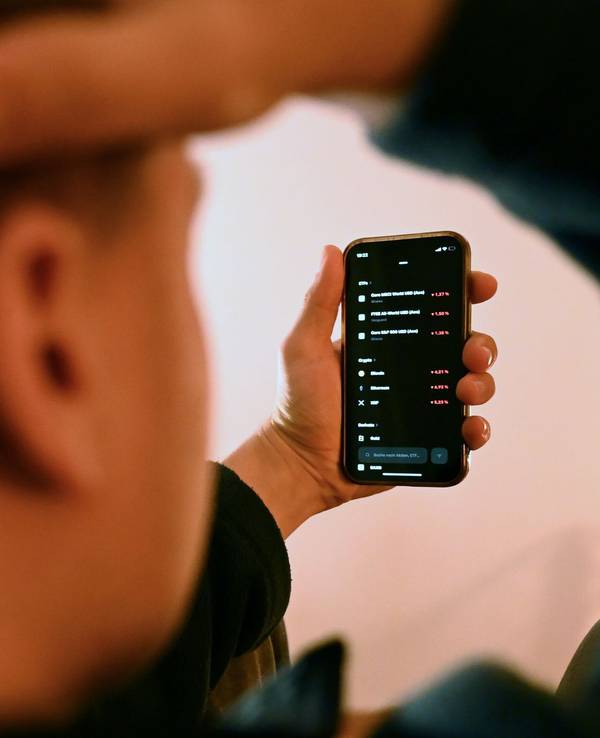Mann schaut sich Trading-App eines Neobrokers mit Aktienkursen an