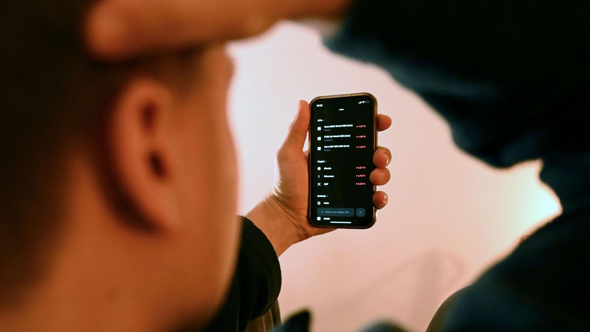 Mann schaut sich Trading-App eines Neobrokers mit Aktienkursen an