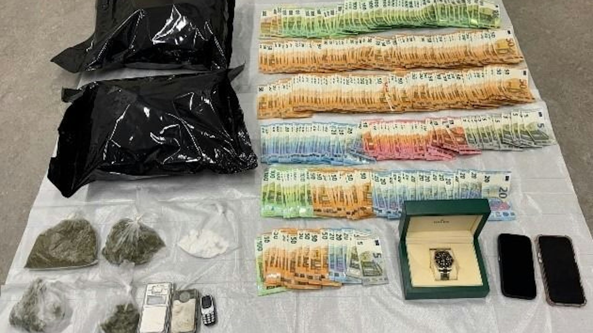 Sichergestellte Drogen, Bargeld und eine Rolex-Uhr liegen auf einem Tisch.