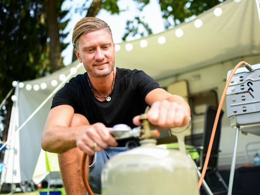 Ein junger Mann schließt eine Gasflasche an einen Gasgrill an
