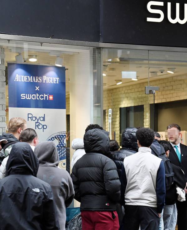 Menschen warten in einer Schlange vor dem Swatch-Store, vor dessen Tür stehen zwei Security-Mitarbeiter.