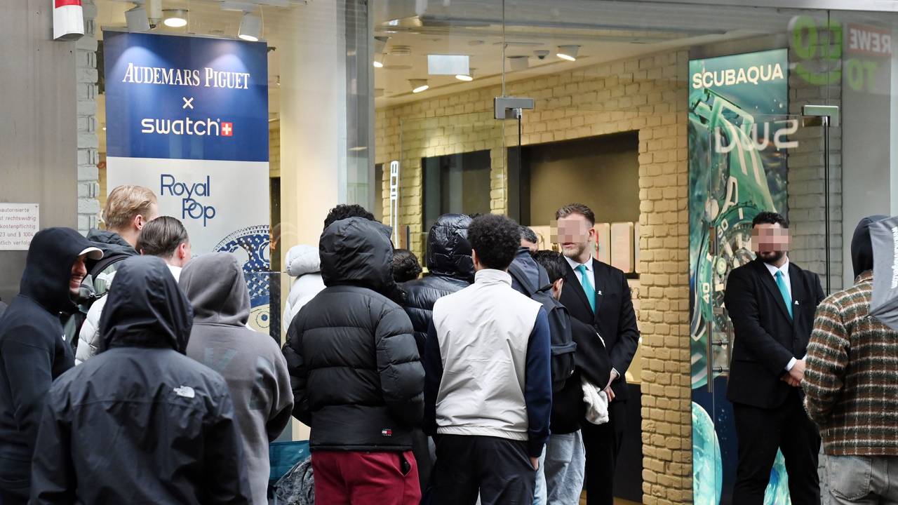 Menschen warten in einer Schlange vor dem Swatch-Store, vor dessen Tür stehen zwei Security-Mitarbeiter.