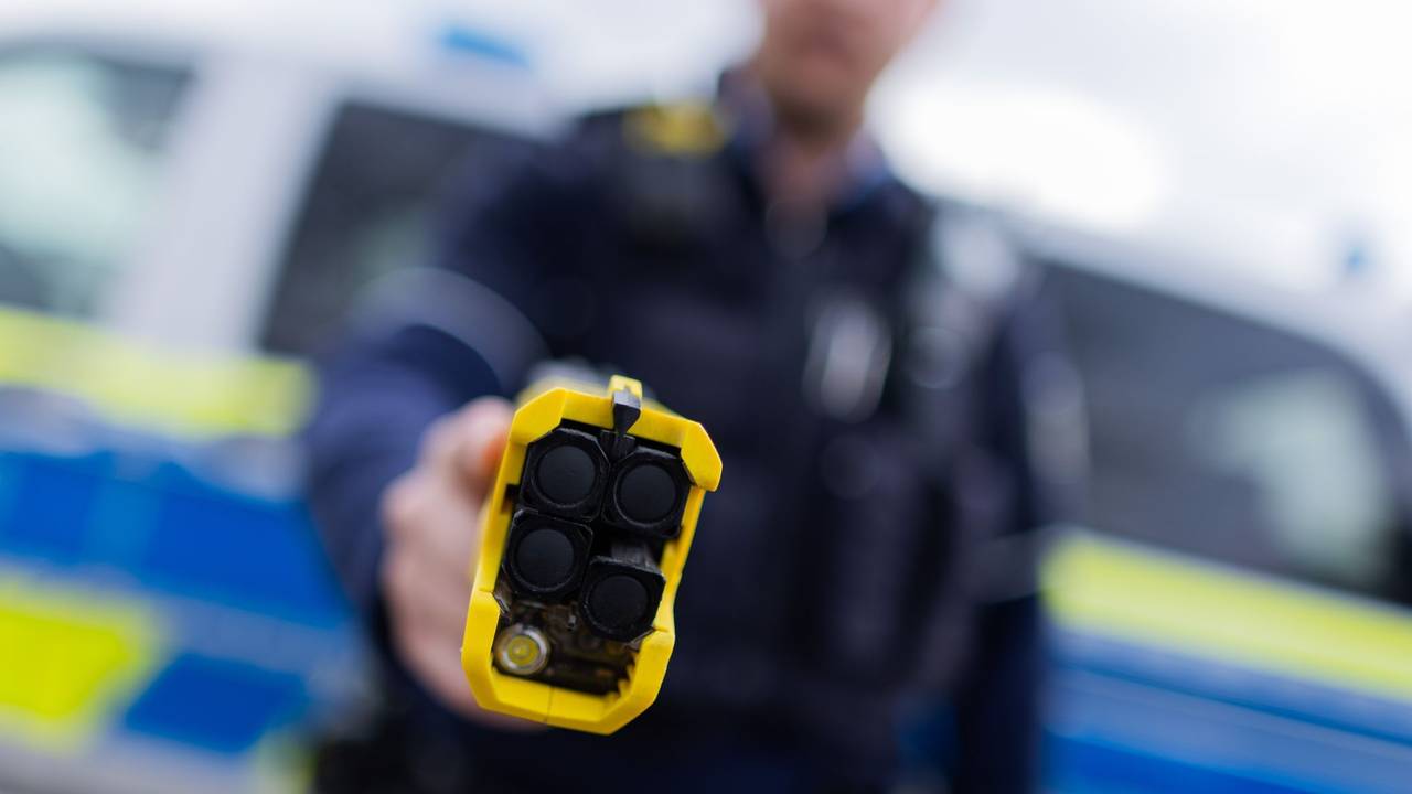 Ein Polizist hält einen Taser in die Kamer.