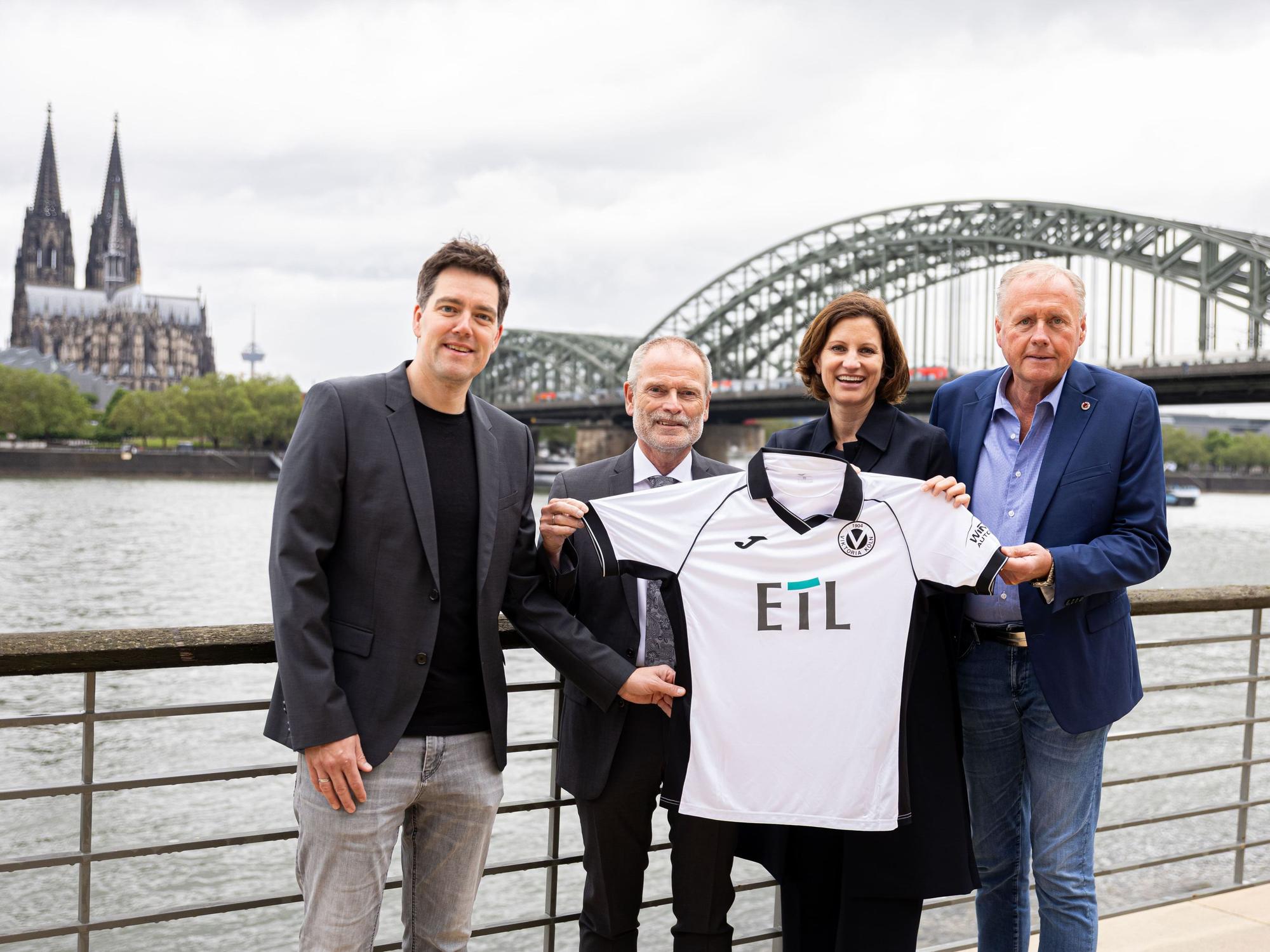 Von links: Axel Freisewinkel (Geschäftsführer FC Viktoria Köln 1904 Spielbetriebs GmbH), Christoph Malzkorn (Vorstand ETL-Gruppe), Nadine Lais (Geschäftsführerin ETL Service GmbH), Eric Bock (Geschäftsführer FC Viktoria Köln 1904 Spielbetriebs GmbH) am Rhein vor dem Dom und der Hohenzollernbrücke.