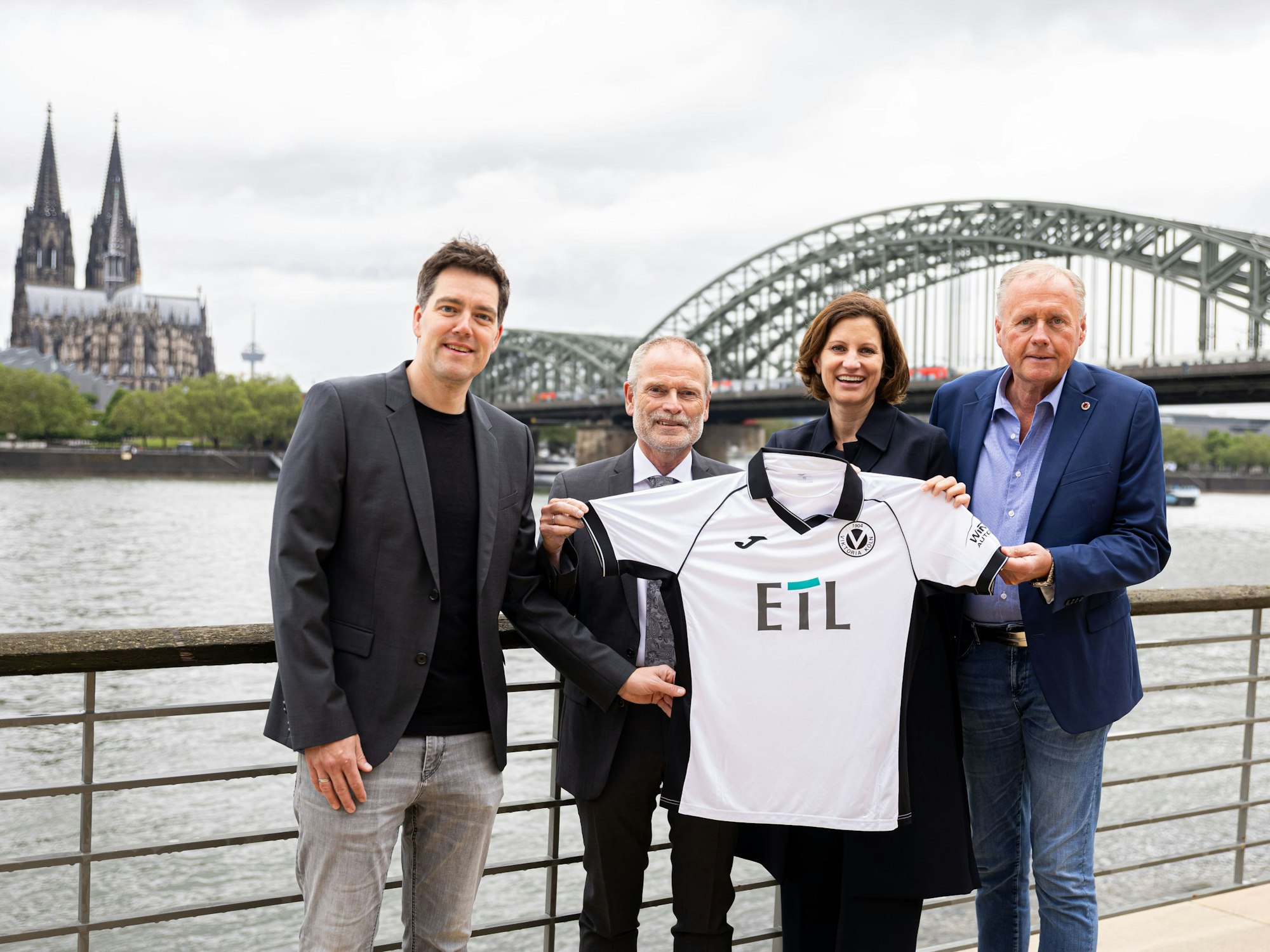 Von links: Axel Freisewinkel (Geschäftsführer FC Viktoria Köln 1904 Spielbetriebs GmbH), Christoph Malzkorn (Vorstand ETL-Gruppe), Nadine Lais (Geschäftsführerin ETL Service GmbH), Eric Bock (Geschäftsführer FC Viktoria Köln 1904 Spielbetriebs GmbH) am Rhein vor dem Dom und der Hohenzollernbrücke.