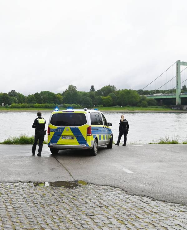 Zwei Polizeikräfte sowie zwei Einsatzfahrzeuge stehen am Rheinufer.
