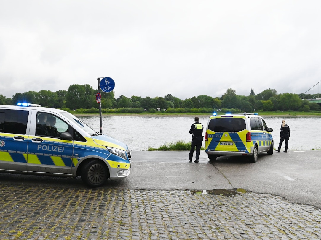 Zwei Polizeikräfte sowie zwei Einsatzfahrzeuge stehen am Rheinufer.