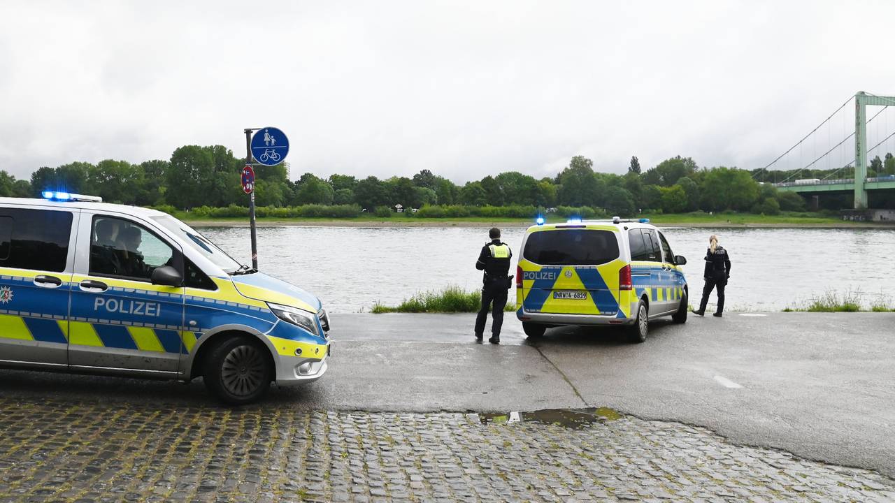 Zwei Polizeikräfte sowie zwei Einsatzfahrzeuge stehen am Rheinufer.