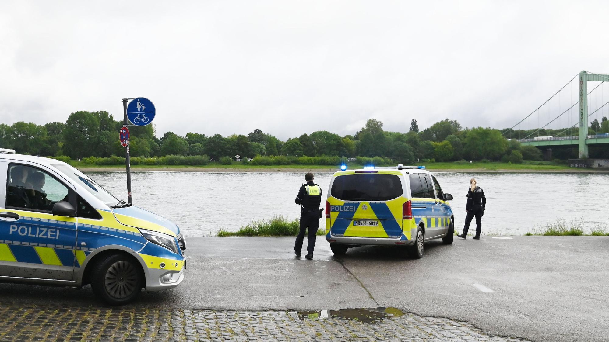 Zwei Polizeikräfte sowie zwei Einsatzfahrzeuge stehen am Rheinufer.