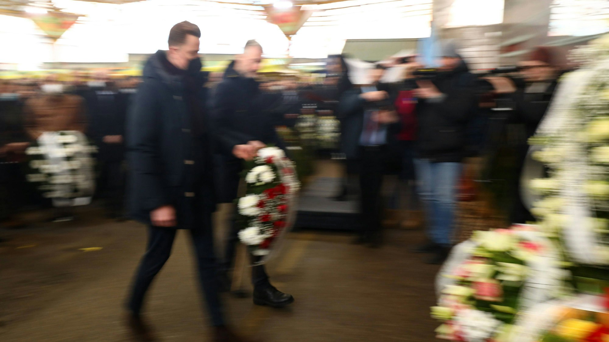 Menschen mit Blumenkränzen bei Gedenkveranstaltung